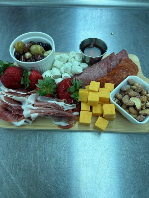 A wooden tray has strawberries, cheese cubes, grapes, nuts, and a small bowl of sauce.