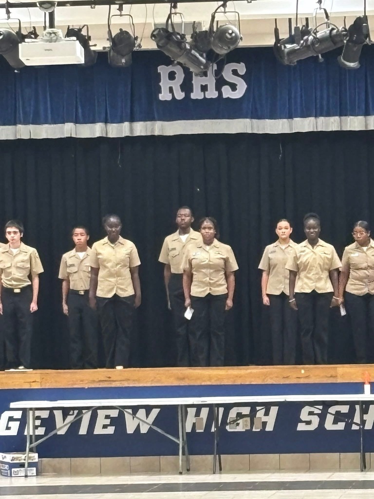 Students in matching uniforms stand on a stage with "RHS" in the background.