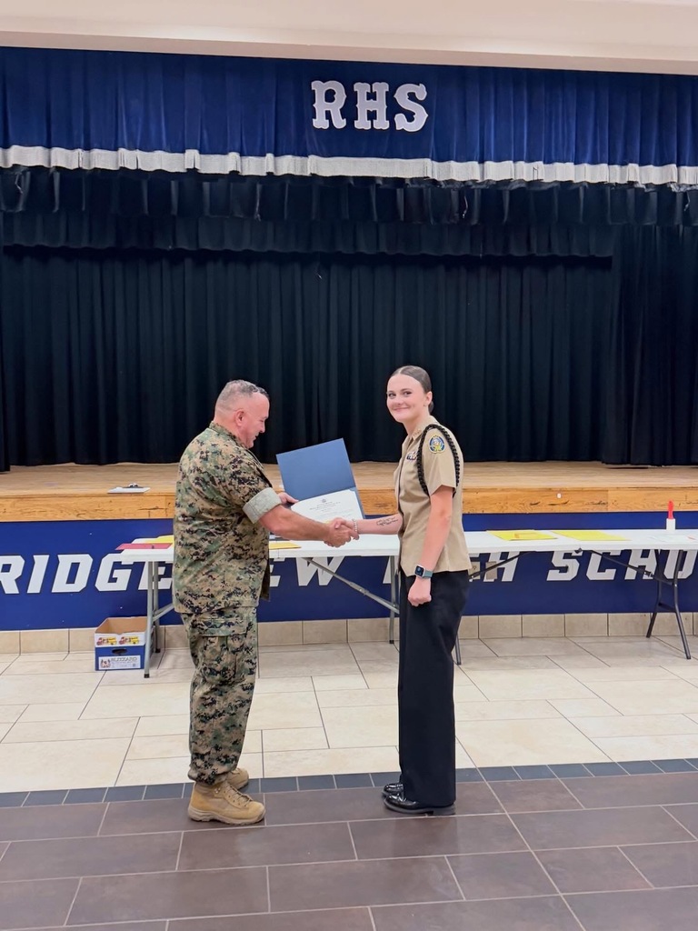 A man in uniform hands a folder to a woman in front of a stage.