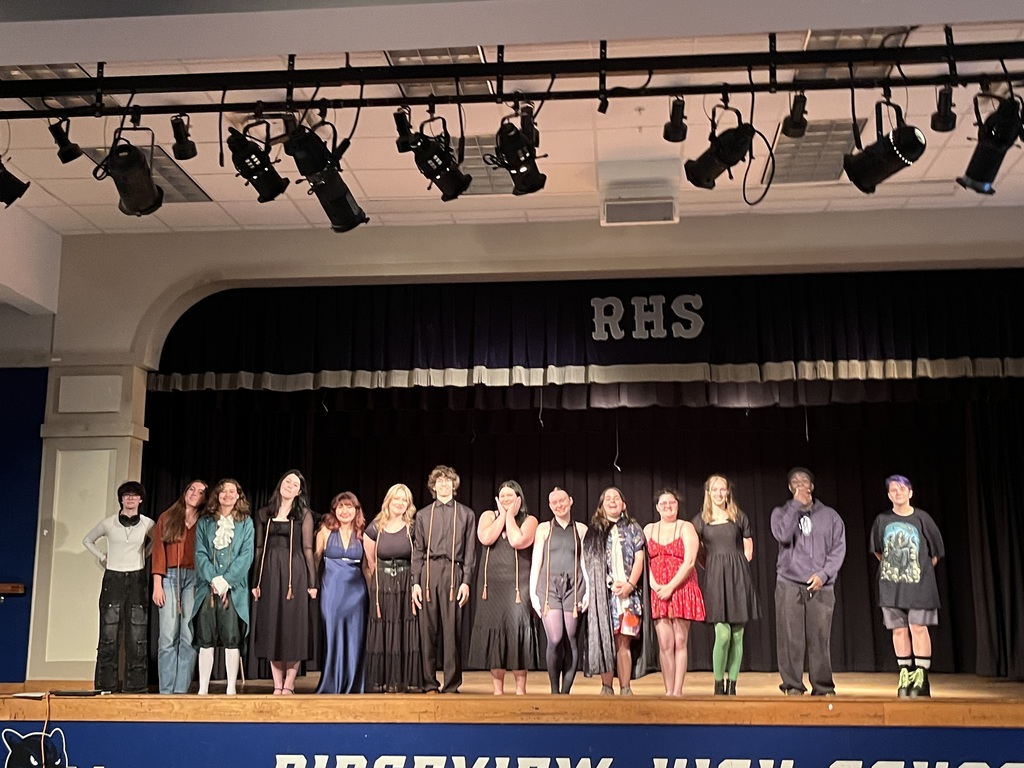 Several people on a stage with spotlights overhead. The sign behind them reads "RHS" and the sign at the bottom says "BIRDVIEW HIGH SCHOOL."