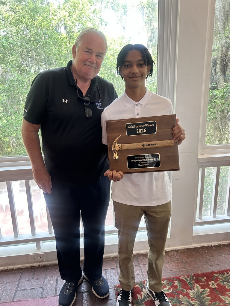 A man and a boy stand in front of a window. The boy holds an award, and the man smiles.