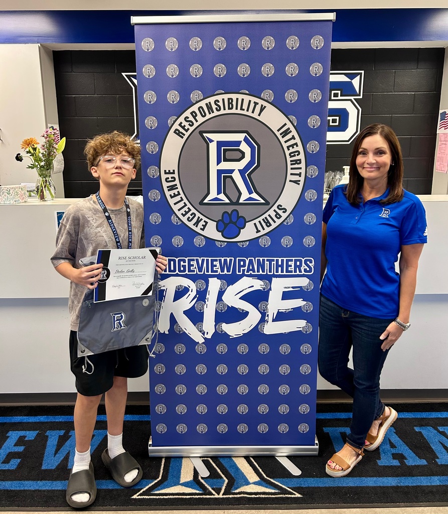 A young boy and an adult woman standing near a blue banner with the words "Rise" and "Ogeview Panthers" on it.