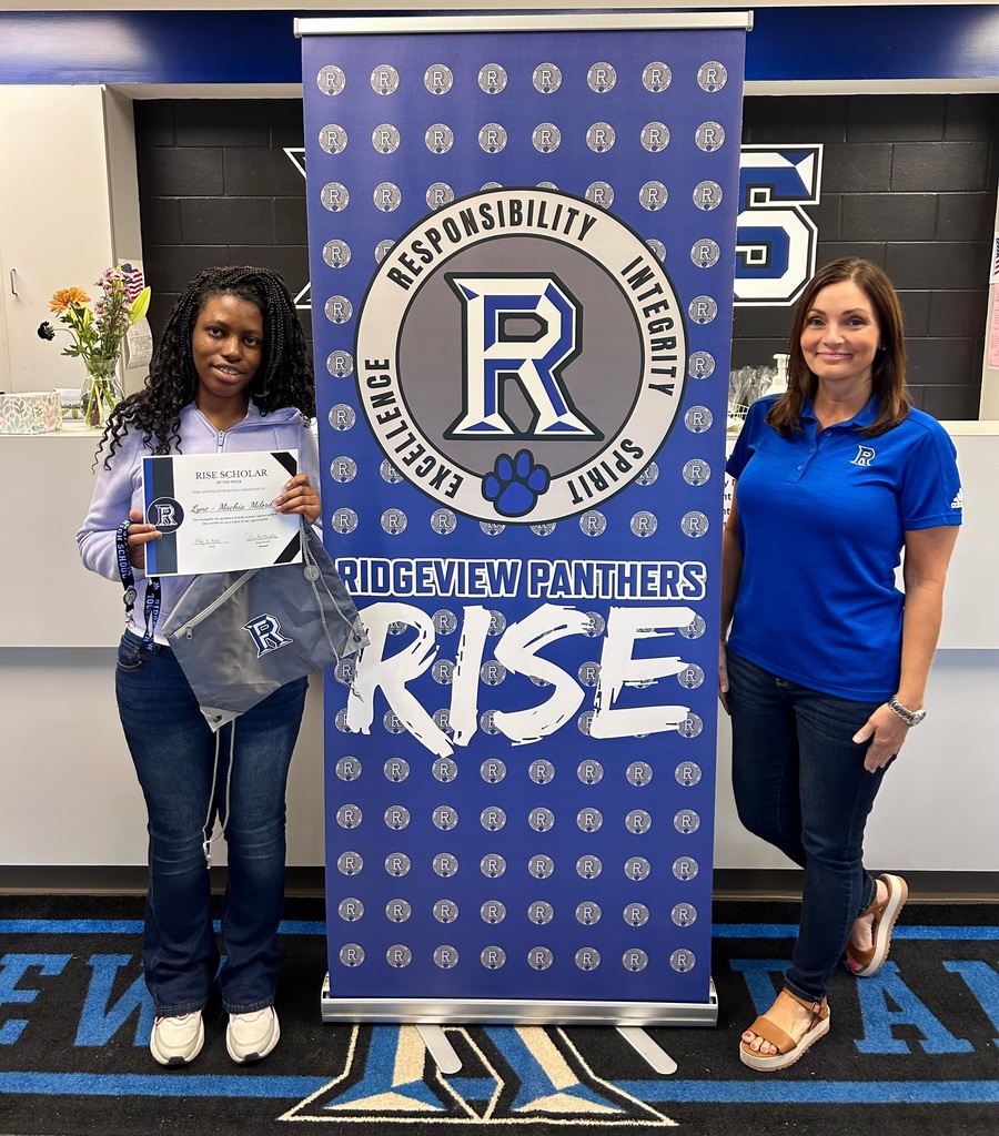 Two women stand by a large blue sign with the letters "R" and "RISE" and a paw print.