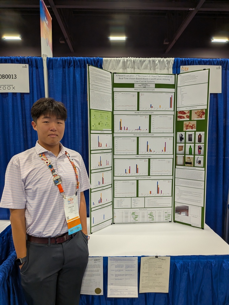 Chun stands in front of an exhibit board with multiple panels, wearing a belt, shirt, and watch.