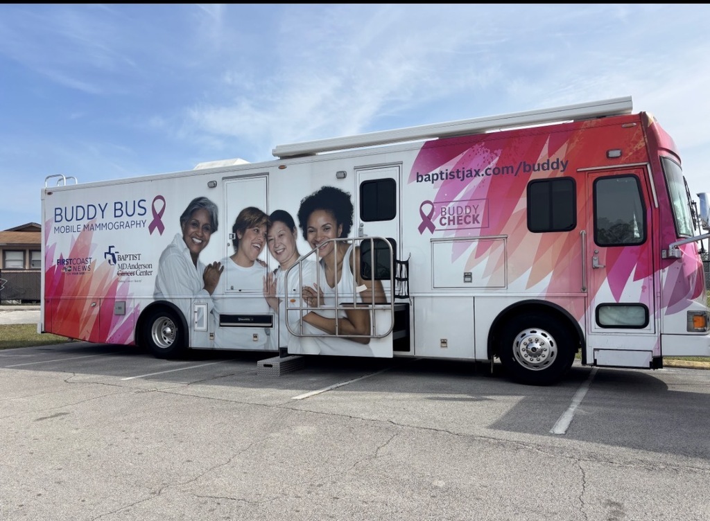 A large pink and white vehicle parked in a lot with pink ribbons and images of women.