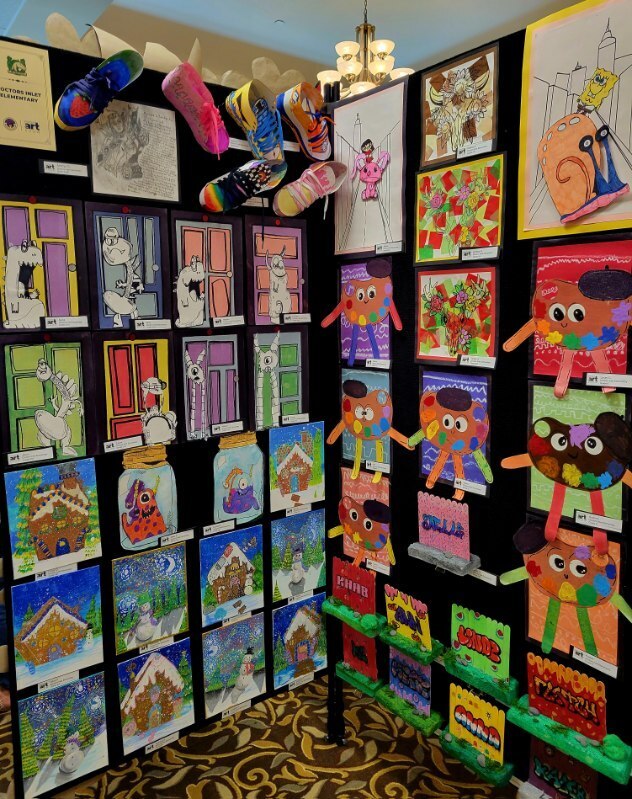 Display of children's artwork on a black wall, featuring various colorful paintings, drawings, and creative sculptures.