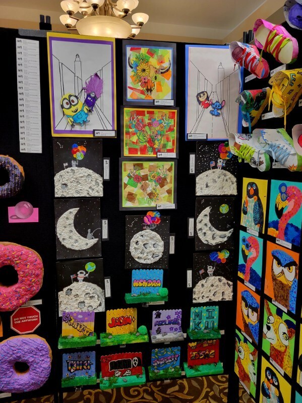 Art pieces on a black wall include drawings of a moon, a cake, and a stop sign. A donut, a stop sign, and a hat are also displayed.