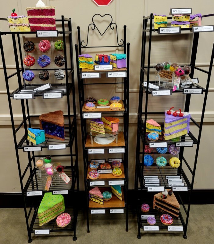 Three black racks display colorful cakes, donuts, and cupcakes. A stop sign is on the wall.