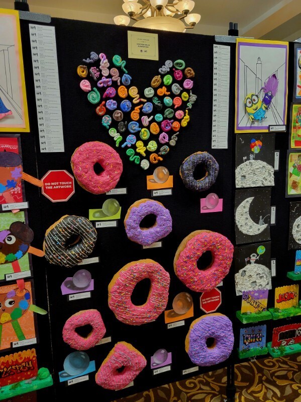 A bulletin board with colorful donut art, a heart made of buttons, and various drawings and paintings in vibrant colors.