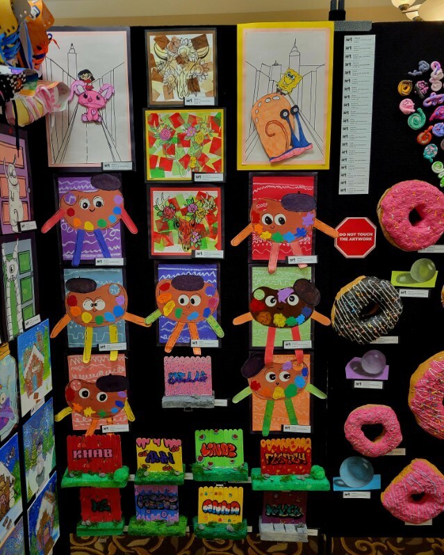 Display of colorful art projects on a black background, featuring characters and donuts. A white stop sign is also visible.