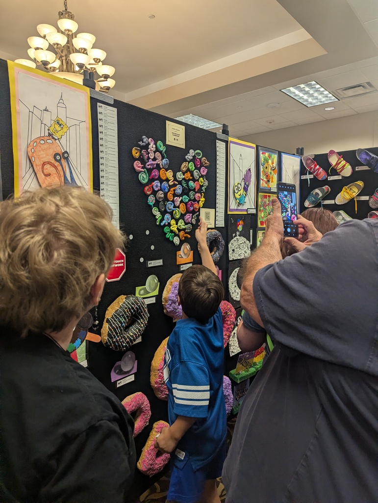 Several people are at an art exhibit, viewing colorful and unique art pieces on the wall.