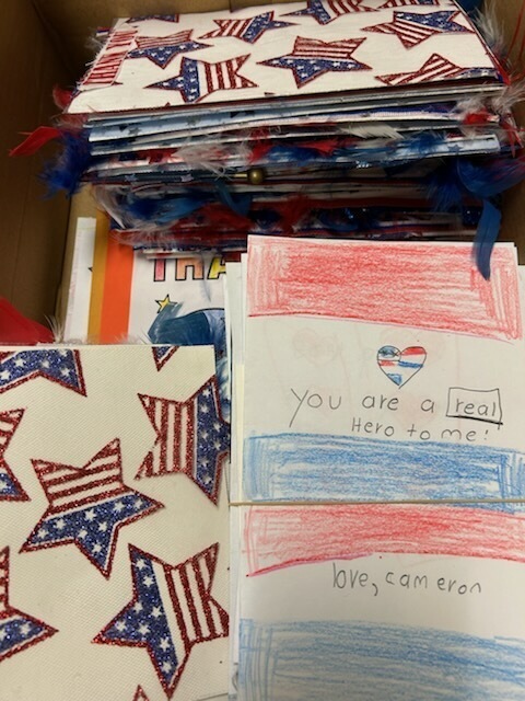 Stacks of handmade cards with American flag designs and handwritten messages, one card says "You are a real Hero to me."