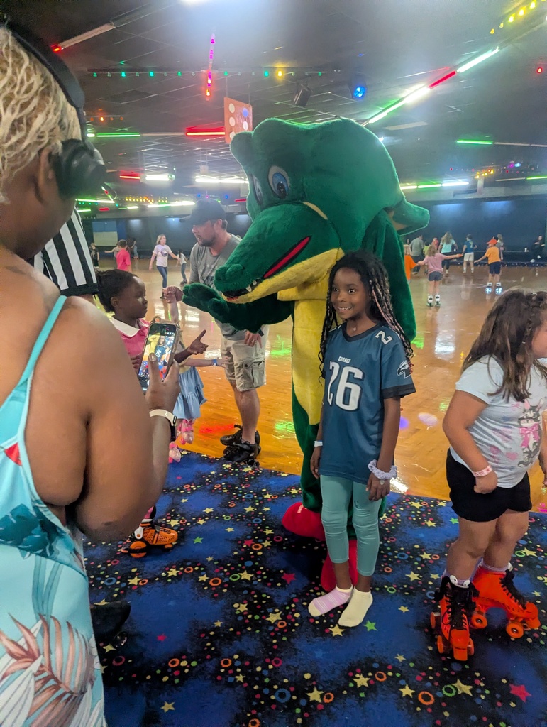 A mascot and young children pose for a photo at a roller rink with a starry floor.