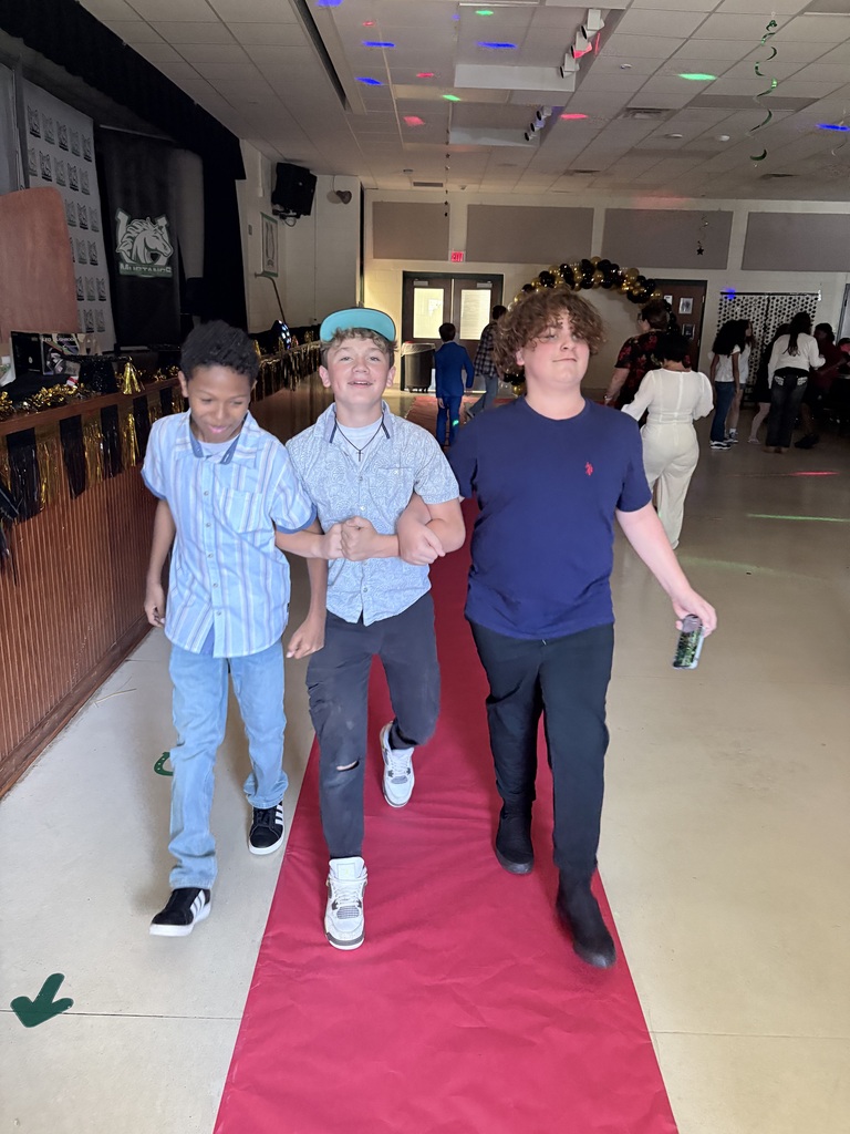Three boys walk together on a red carpet in a hallway. They are dressed casually.