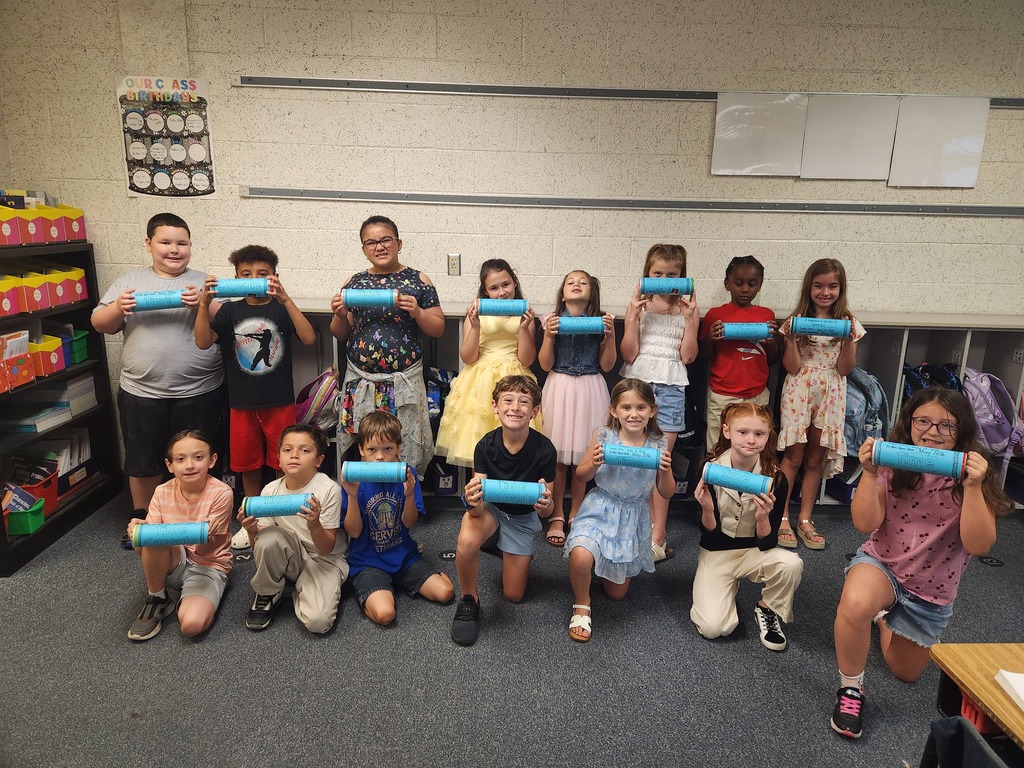 A classroom with kids in various outfits holding blue cylinders, posing for a photo.