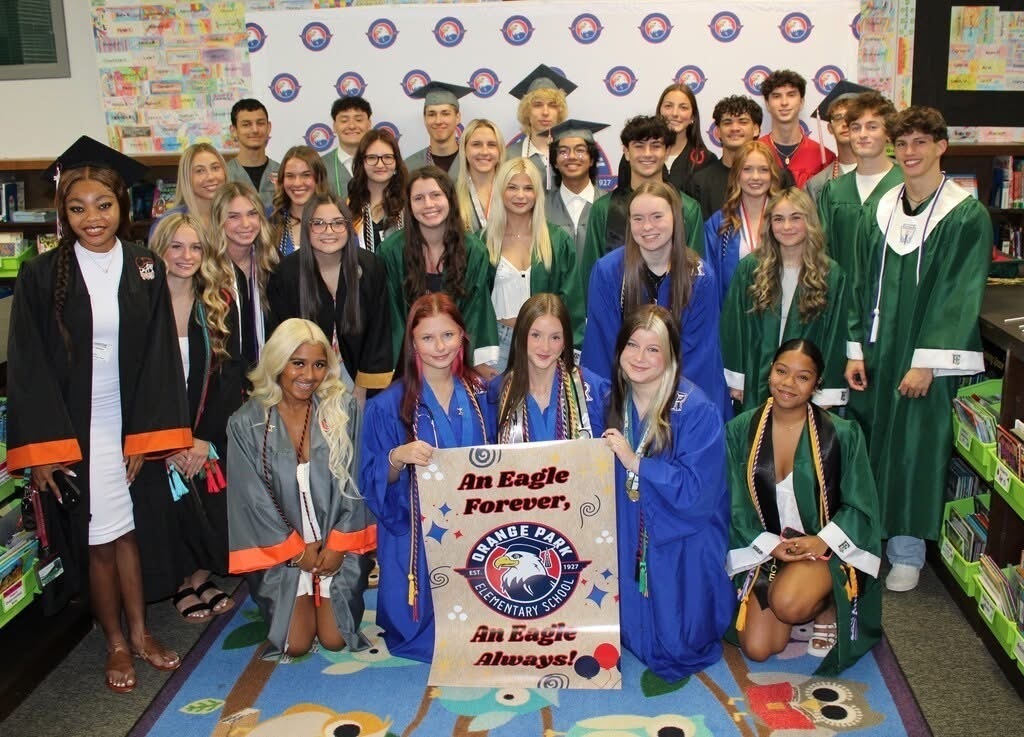 A classroom with a group of students in graduation gowns. Some hold a banner that reads "An Eagle Forever".