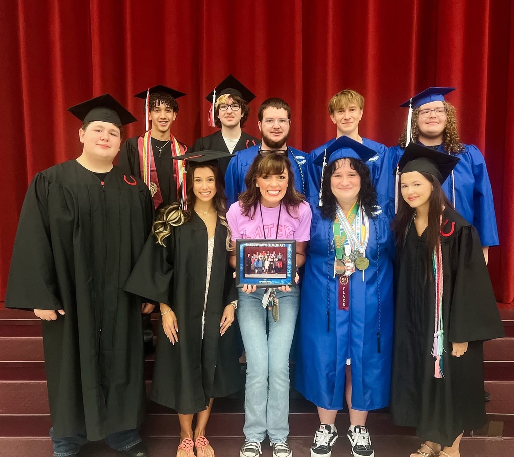 People in caps and gowns posing for a photo at a graduation ceremony with a red backdrop.