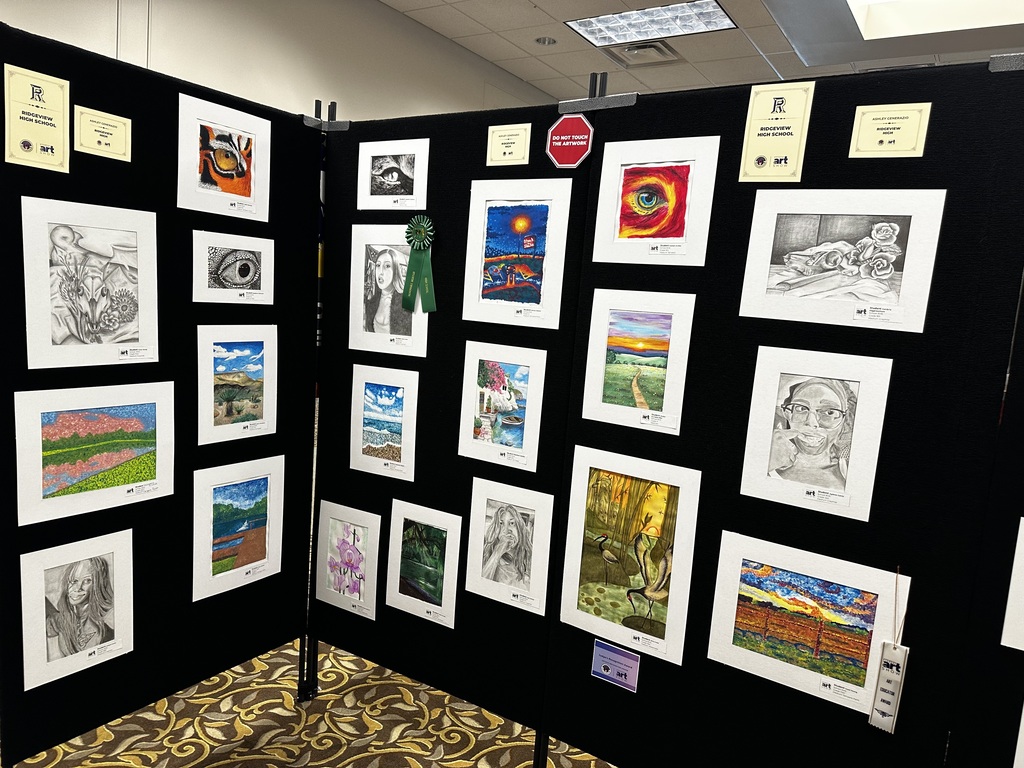 A black wall displays numerous framed artworks, with a mix of black and white, colorful images, and a stop sign.