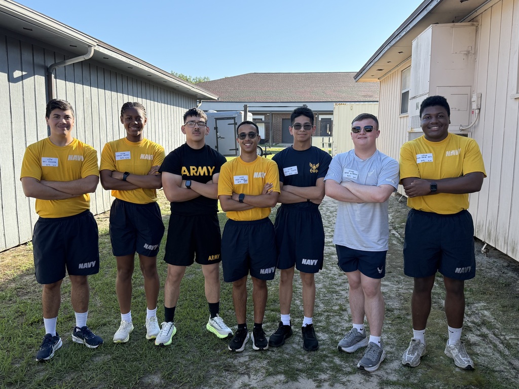 Seven young people wearing yellow and blue uniforms and sneakers standing in a row in front of buildings.