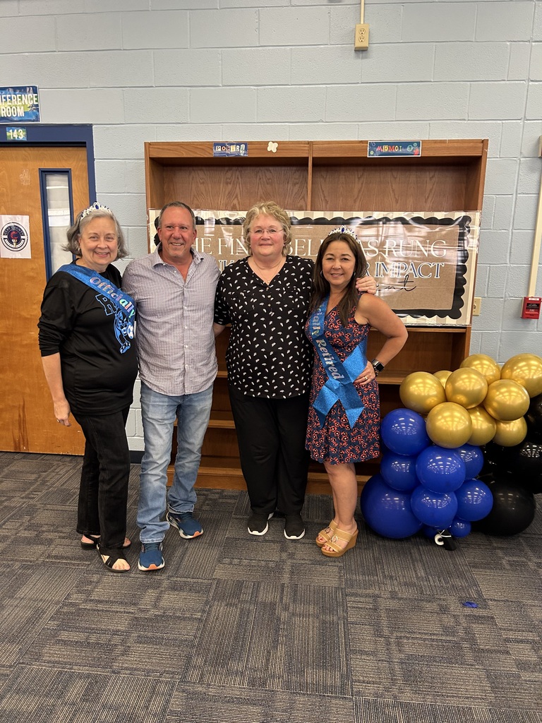 Four people in front of a room with blue and gold balloons, a bookshelf, and a door.
