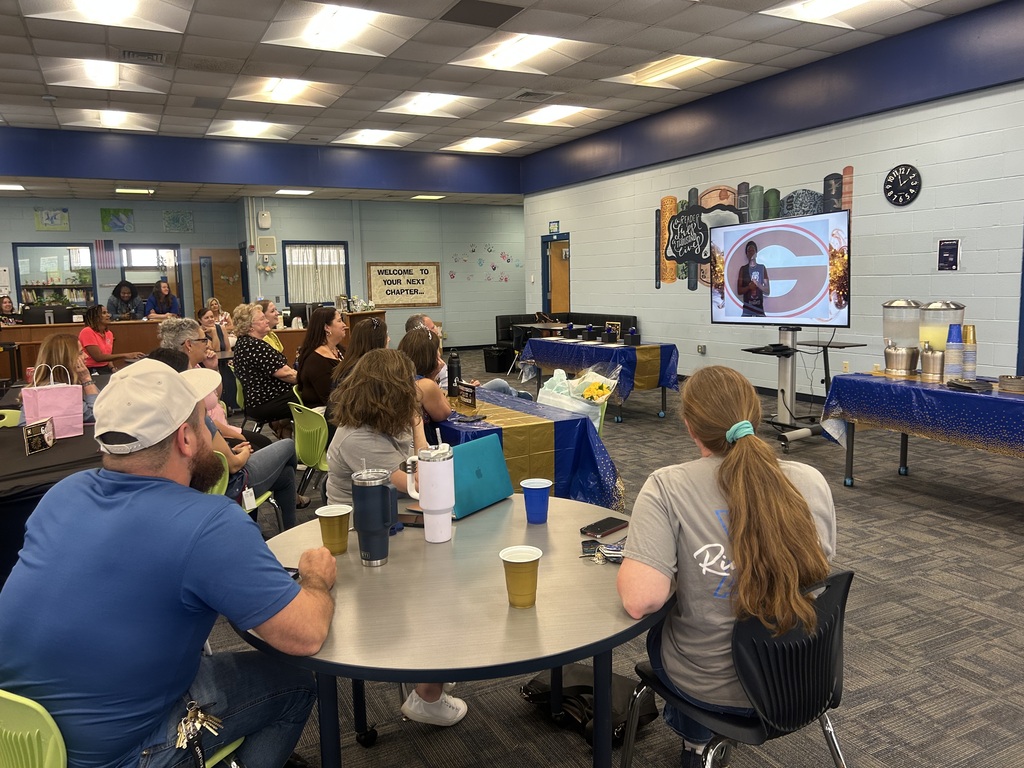 People sit at tables in a room with blue walls, white ceiling, and a projector screen.
