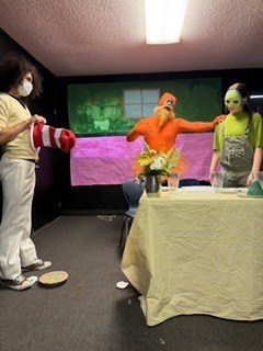 Three people stand in a room with a large screen in the background. One holds a red and white striped object.