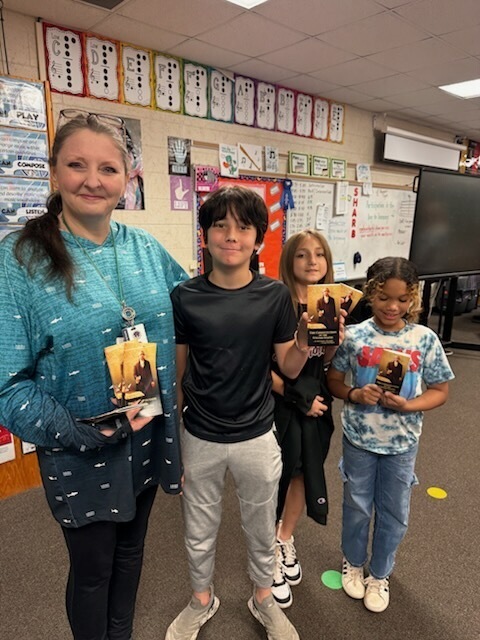 A woman and three children hold awards and pose for a photo in a classroom.
