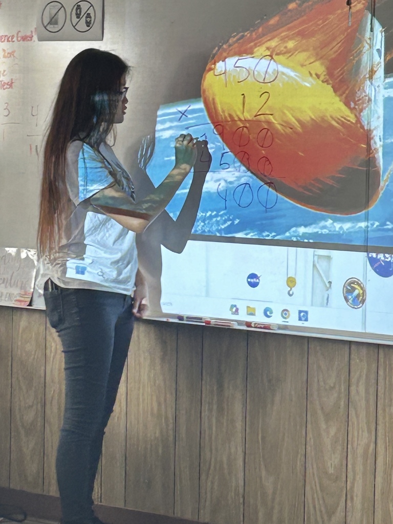 A woman in a white shirt and jeans writes on a whiteboard displaying an image of a sun.
