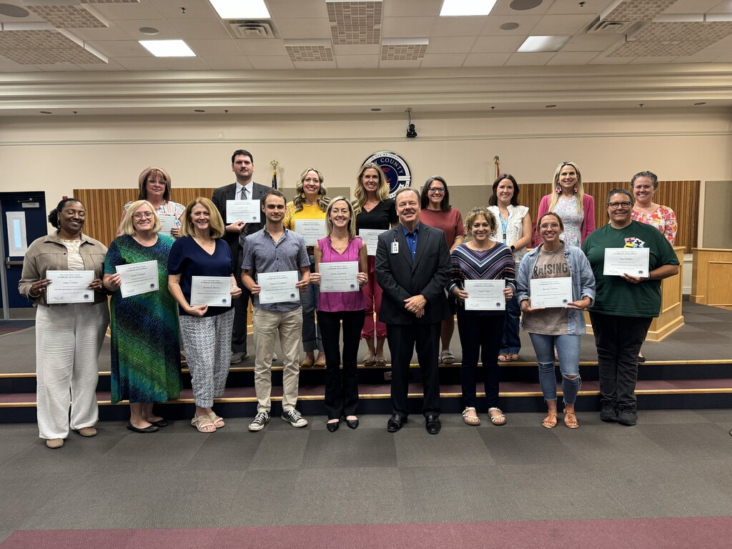 The Superintedent and the Teacher Advisory Council stand in a room holding certificates.