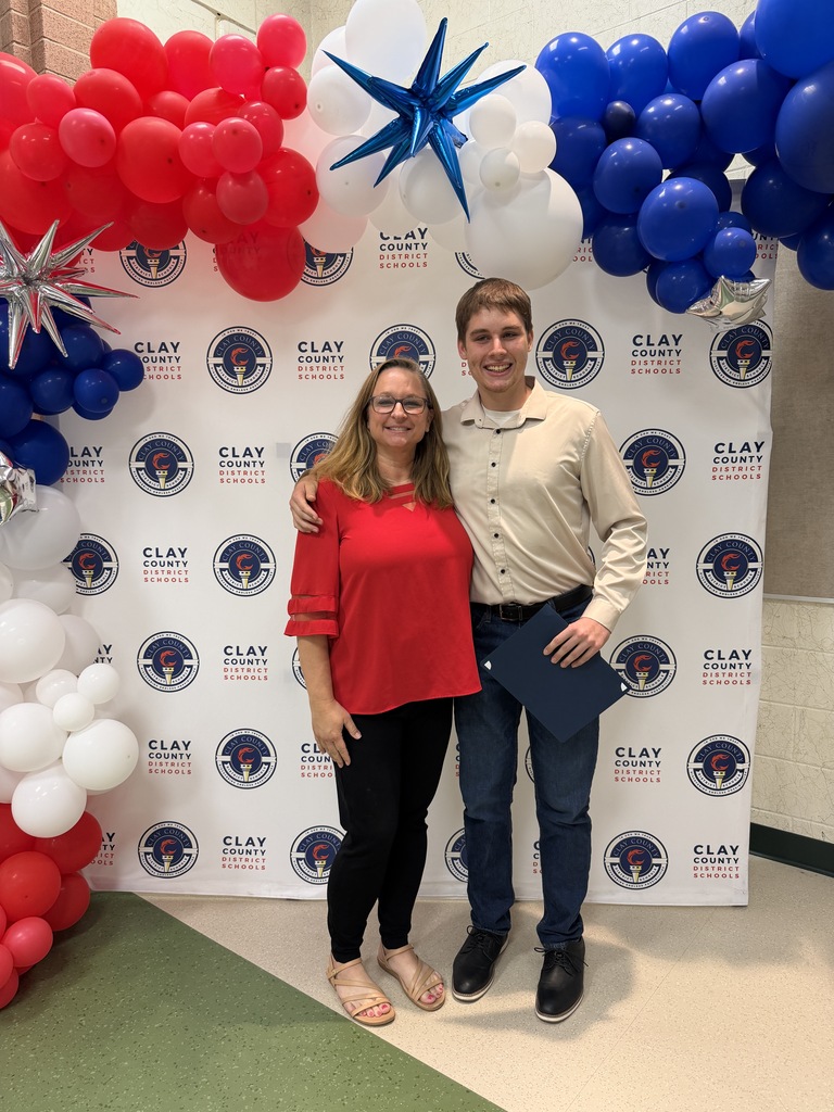 Two people standing before a wall with a patriotic theme, red, white, and blue balloons.