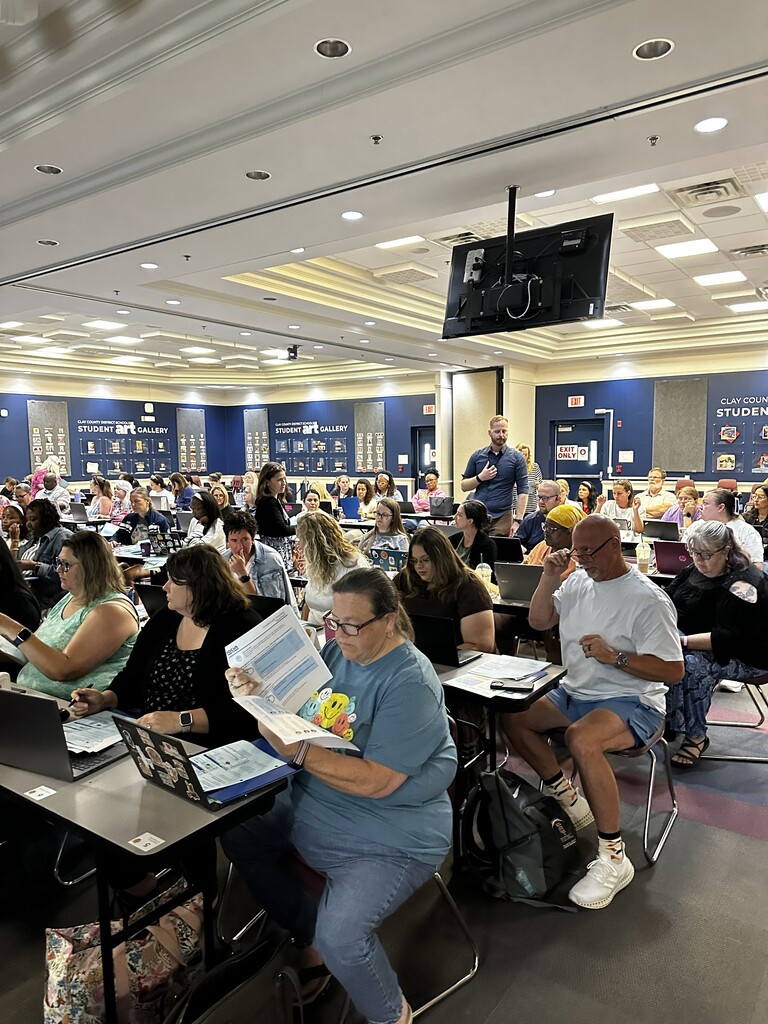 Indoor room with many people sitting at desks with laptops. 