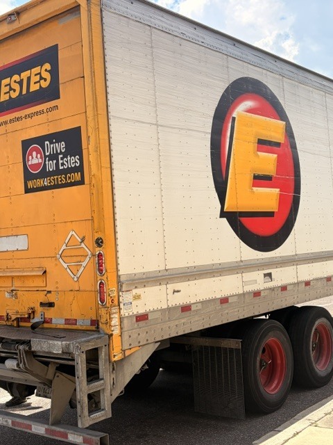 Back of a yellow semi-trailer truck with "ESTES" logo and text. Large yellow "E" on side.