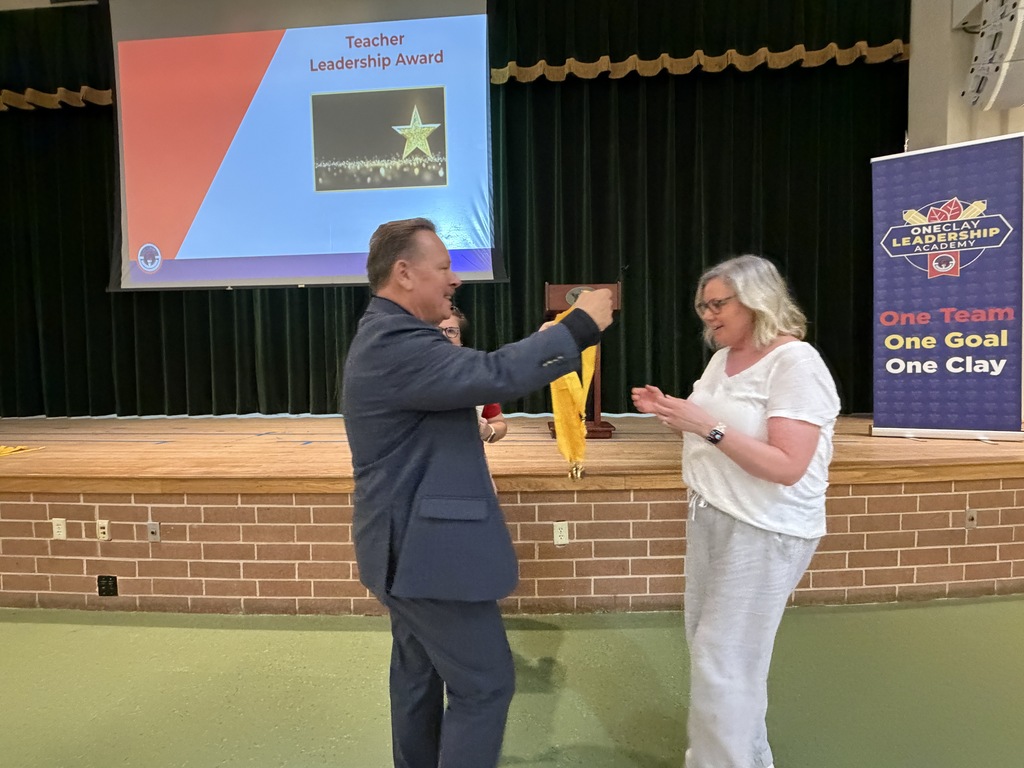 A man and a woman on stage receiving an award; a projector screen behind them displays "Teacher Leadership Award".