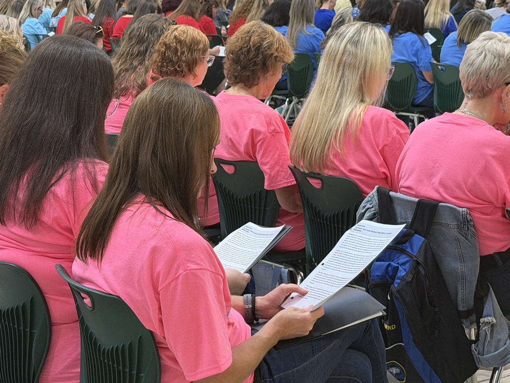 A group of women in pink shirts are seated, reading.