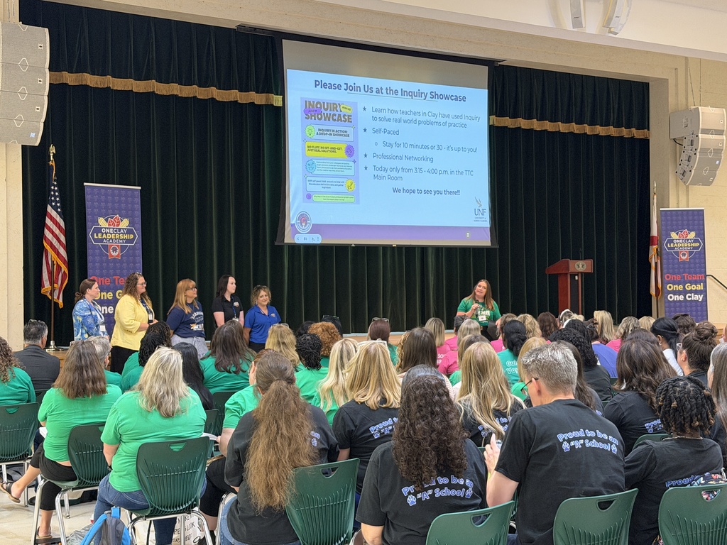 People in green t-shirts sit in chairs facing a projector screen with text, listening to a presentation.