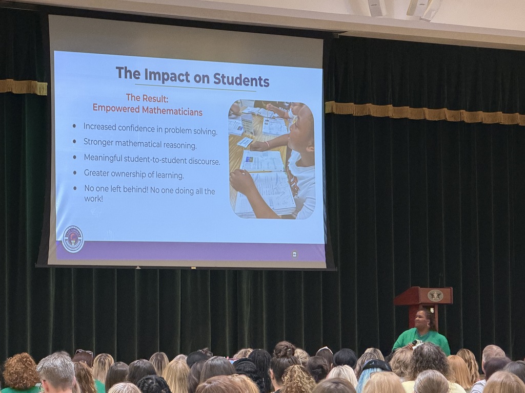 Presentation projector displays "The Impact on Students" on a screen in a dark room. A person speaks at a podium.