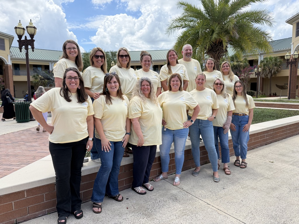 A group of people in yellow shirts and blue jeans pose for a picture outside a building.