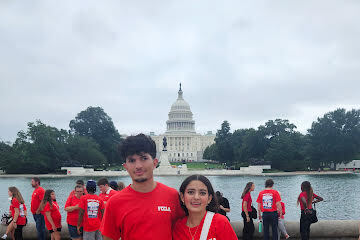 A group of people in red shirts pose in front of a large body of water with the Capitol dome in the background.