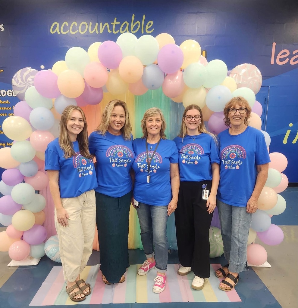 Five women in blue t-shirts pose for a photo in front of a balloon arch.