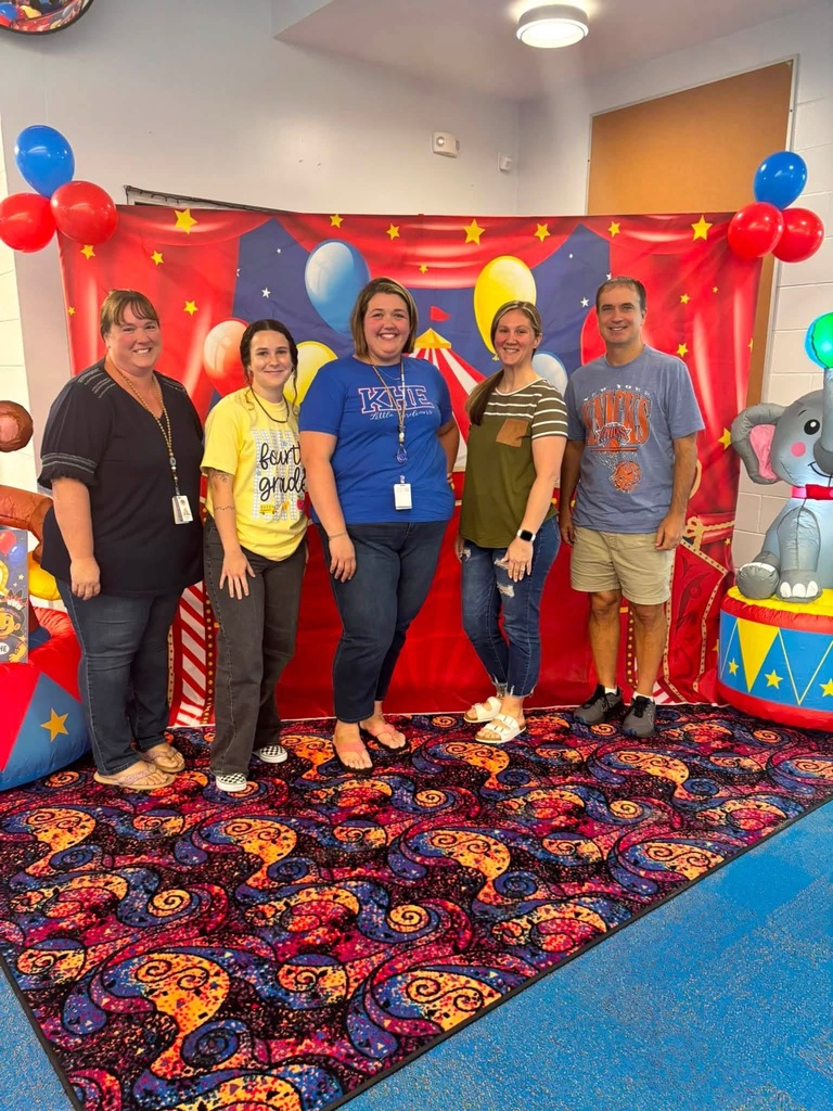 Five people stand together in front of a colorful circus-themed backdrop with balloons.