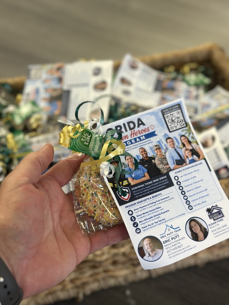 Hand holding a small bag of cookies with a card. Card features photos of people and text. Basket filled with similar cookie bags in the background.