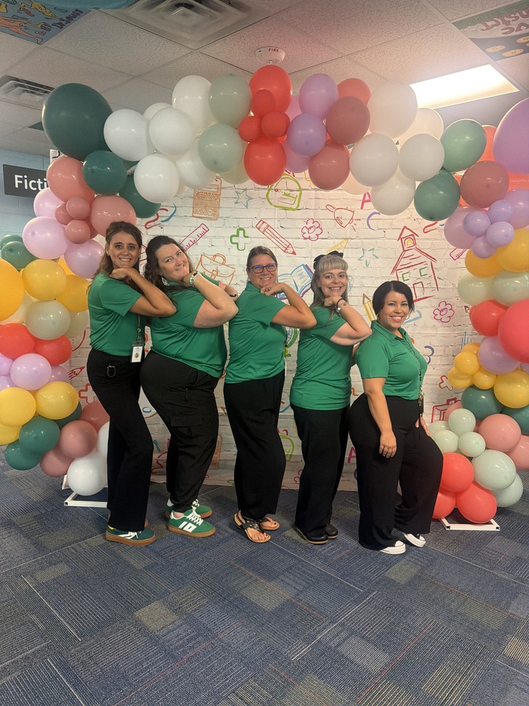 Five people in green shirts and black pants pose in front of a colorful balloon arch.