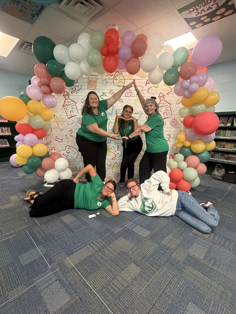 Five people, wearing green shirts, posing for a picture in front of a colorful balloon arch.