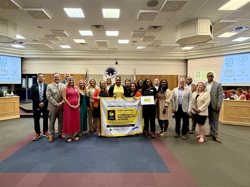 A group of people stand together, holding a yellow and black banner, in a room with wooden panels and a carpeted floor.