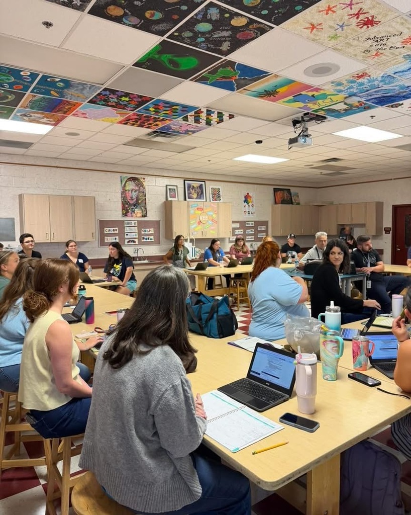 People sitting at tables in a room with a ceiling adorned with colorful artwork.