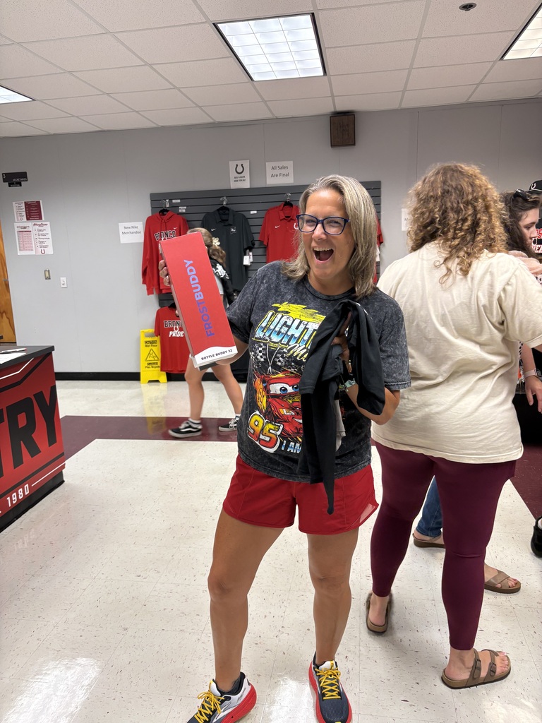 Woman in red shorts holds a red folder, smiling at camera, in a hallway with white walls and red floor.