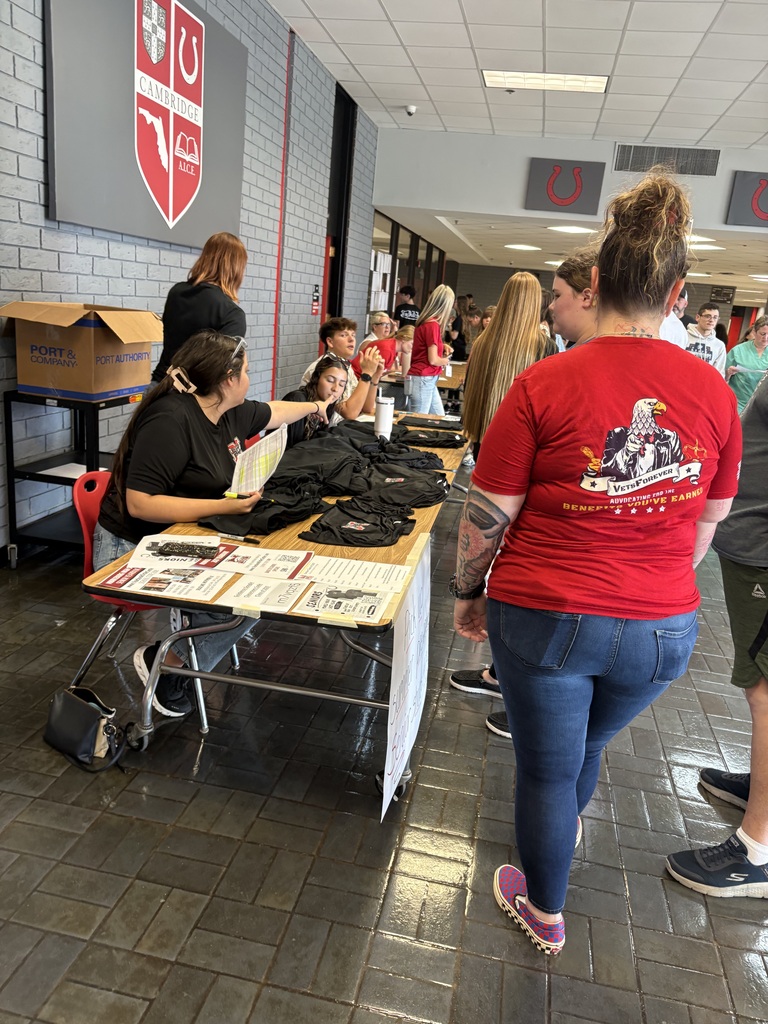 A group of people are gathered around a table with various items on it, inside a hallway.