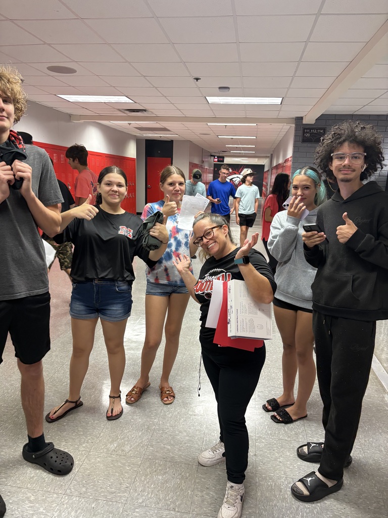 A group of individuals are standing in a school hallway, smiling and posing for a photo.
