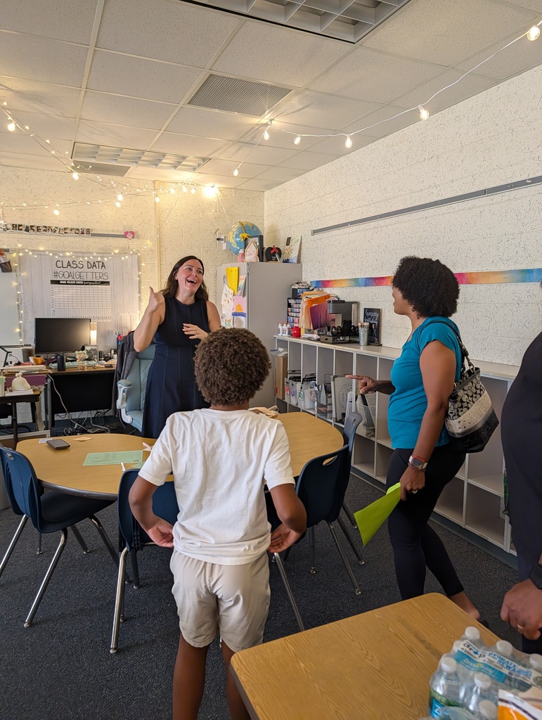 Three adults and a boy in a classroom. A woman talks to the boy who faces away.
