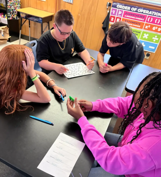 Four students around a table with a puzzle and pens. A girl has her head down.